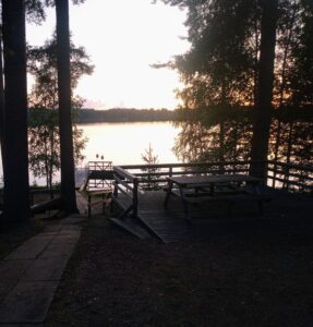 Maisemakuva järvenrannasta, laiturilta, jonka ympärillä kasvaa isoja mäntyjä.