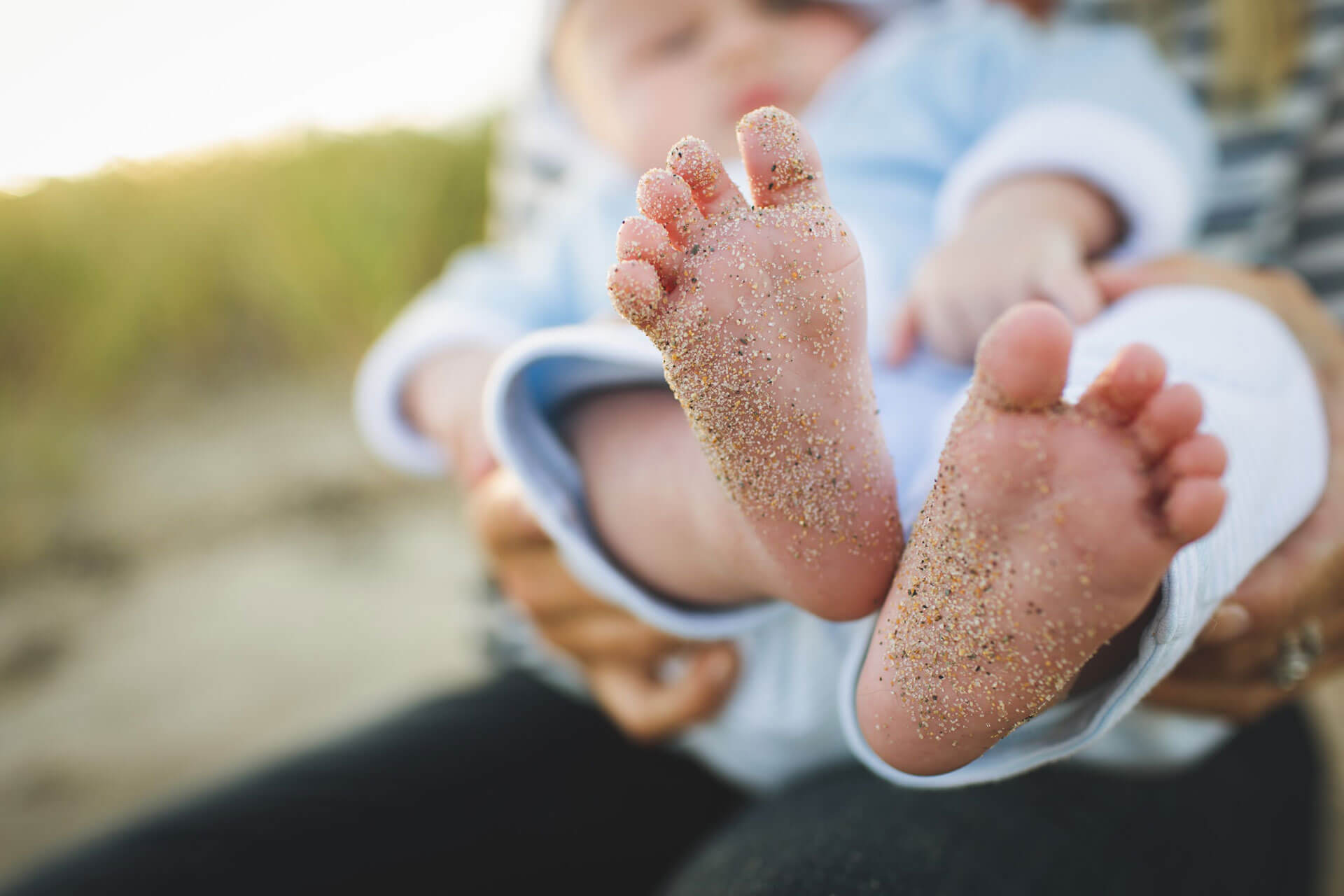 Kuvassa on vauva naisen sylissä ja kuva tarkennettu vauvan hiekkaisiin jalkoihin