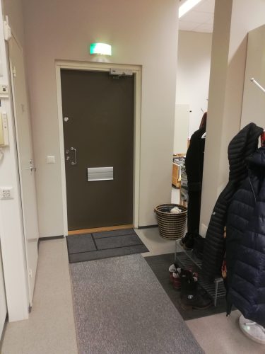 Simpukan toimiston ovi sisältä päin katsoen. Ovesta toimistolle saapuessa vasemmalla naulakot ja kenkäteline, oikealla vessan ovi.